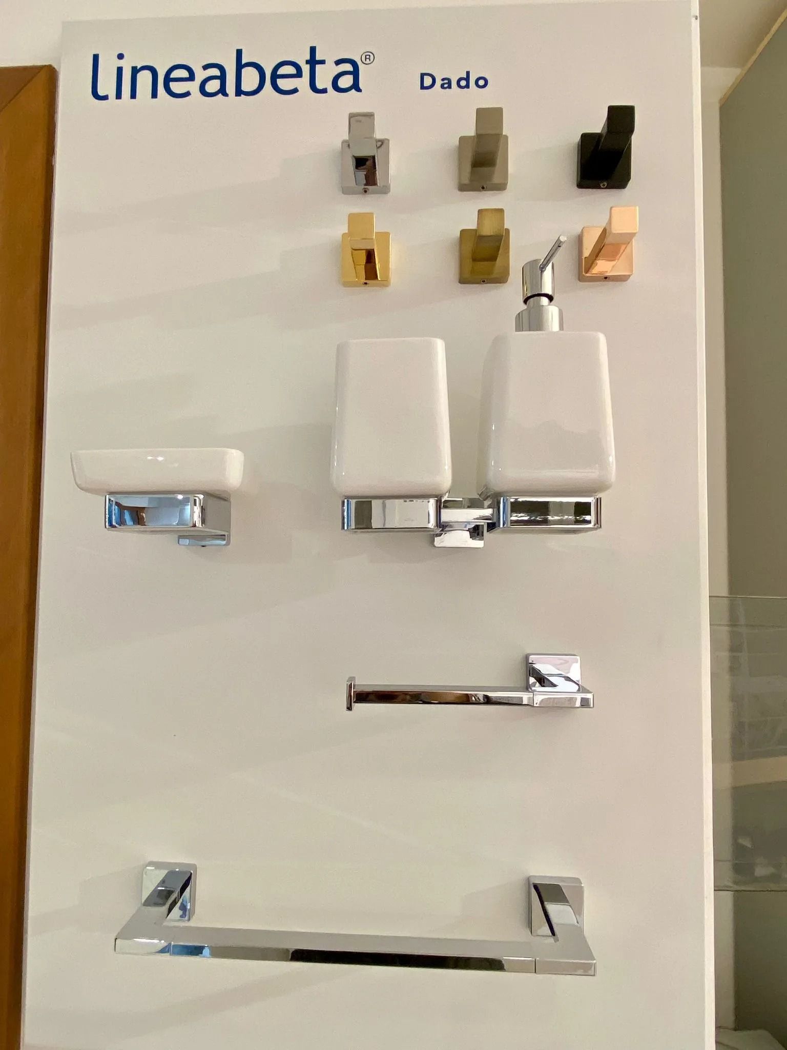 Esposizione di rubinetti e portasciugamani per il bagno su una parete di uno showroom, nelle finiture bianca, cromata e beige.