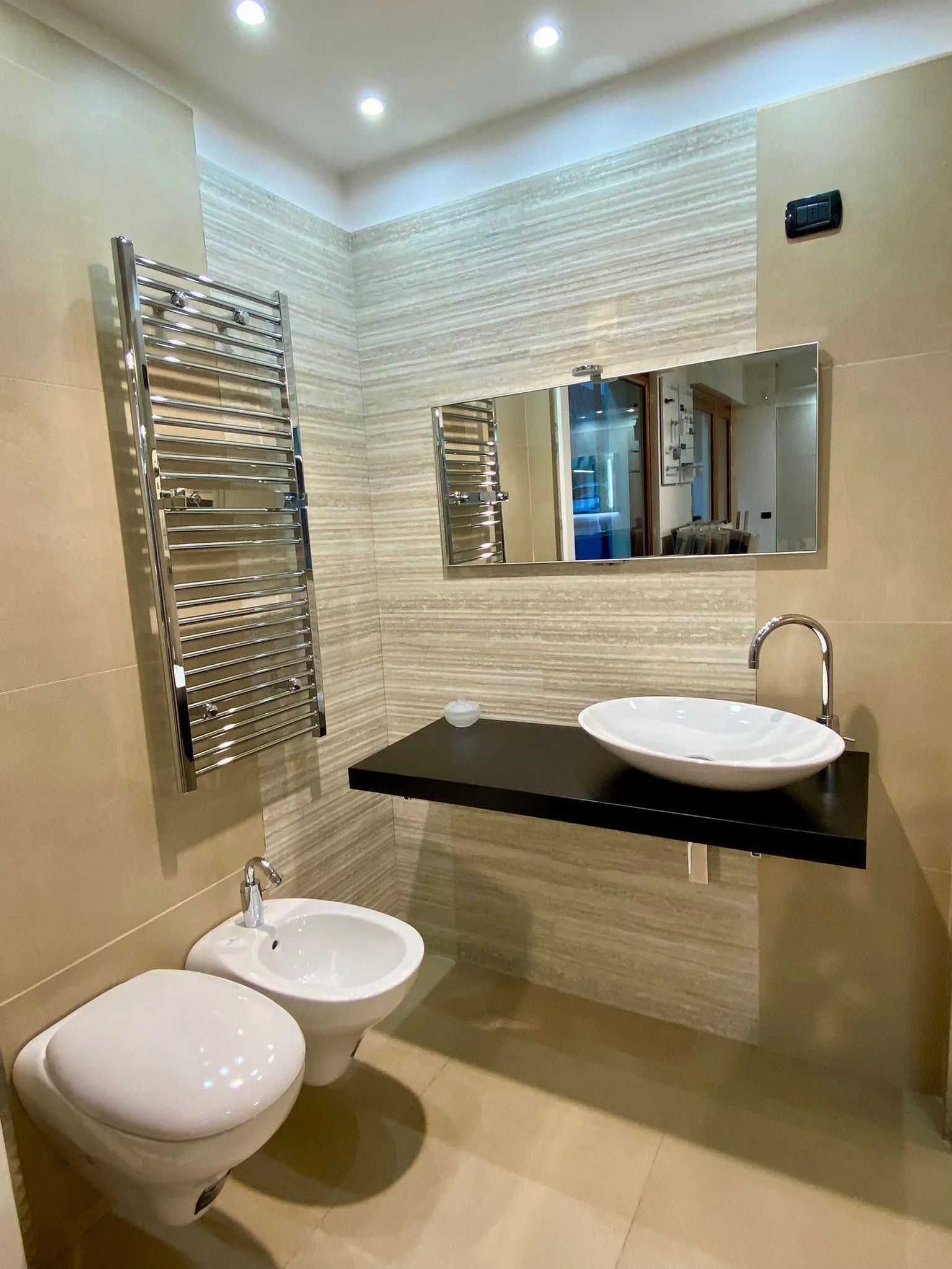 Bagno moderno con lavabo a parete, specchio, portasciugamani e bidet accanto al WC.