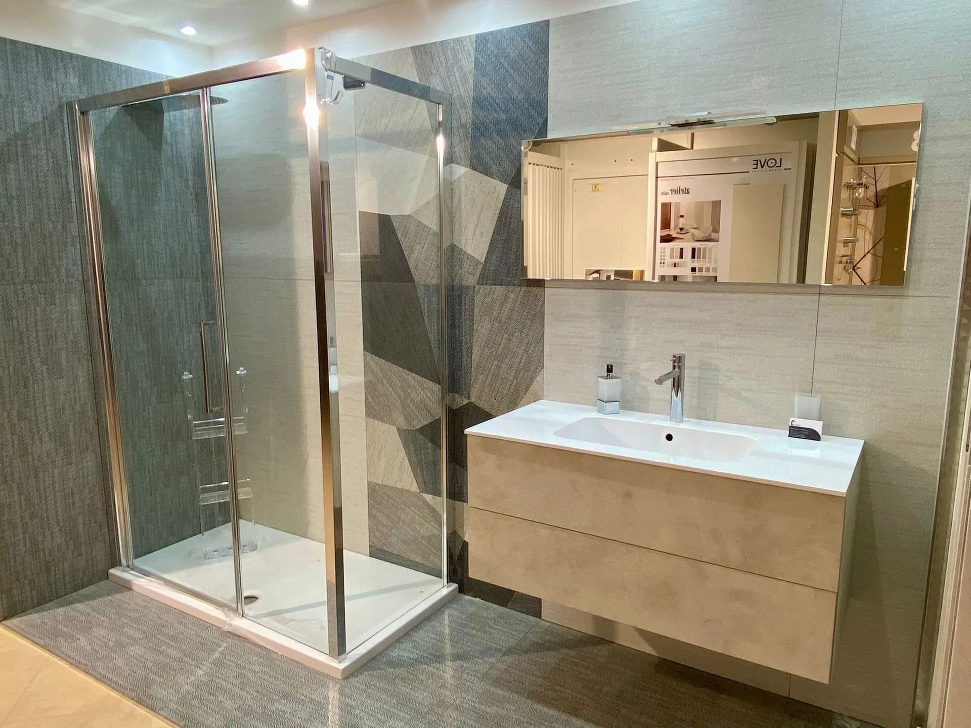 Bagno moderno con doccia in vetro, pareti piastrellate beige e mobile lavabo sospeso con specchio integrato.