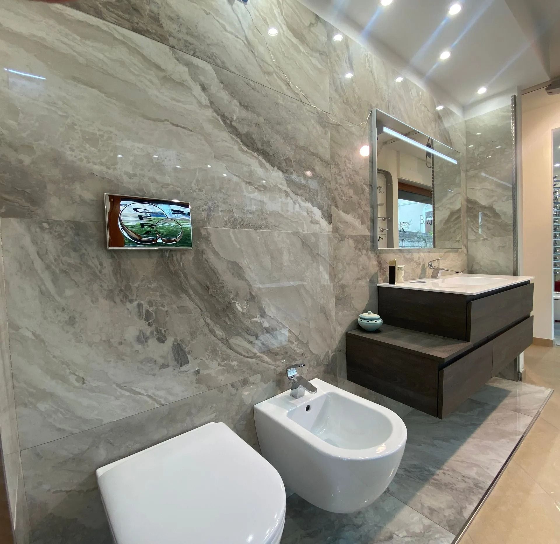 Bagno moderno con pareti in pietra, WC e bidet sospesi, mobile lavabo e specchio illuminato in un elegante interno in stile hotel.