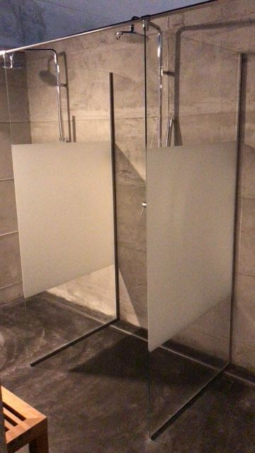 Due cabine doccia con divisori in vetro smerigliato in un bagno, infissi in metallo e pareti in cemento grigio.