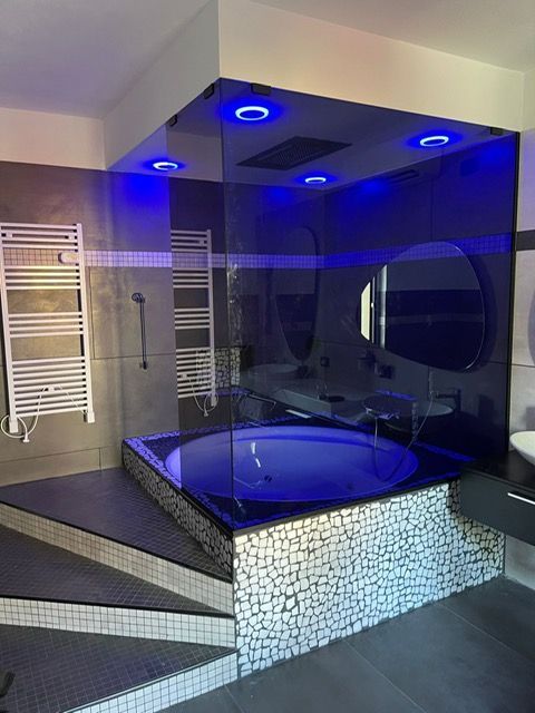 Bagno moderno con vasca da bagno incassata, piastrelle a mosaico e illuminazione blu.