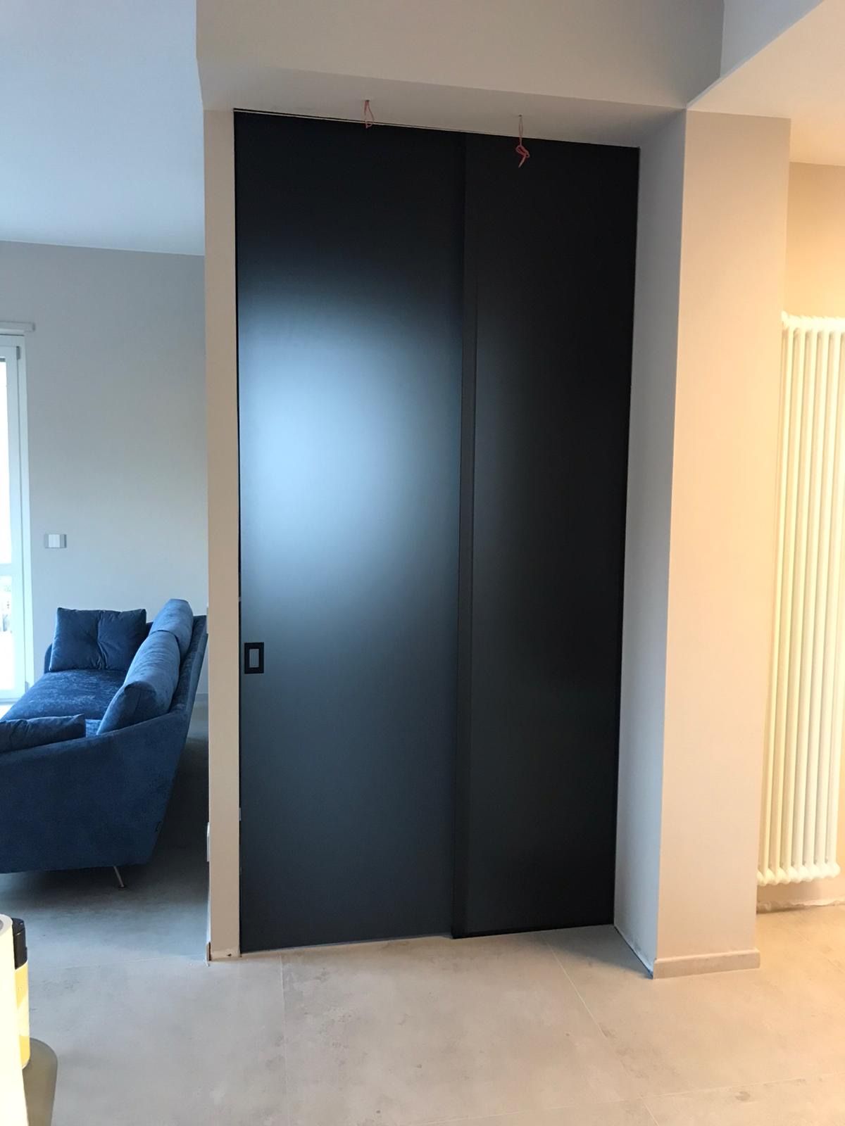 Porta scorrevole nera in un soggiorno moderno; accanto a un pilastro bianco, sullo sfondo c'è un divano blu.