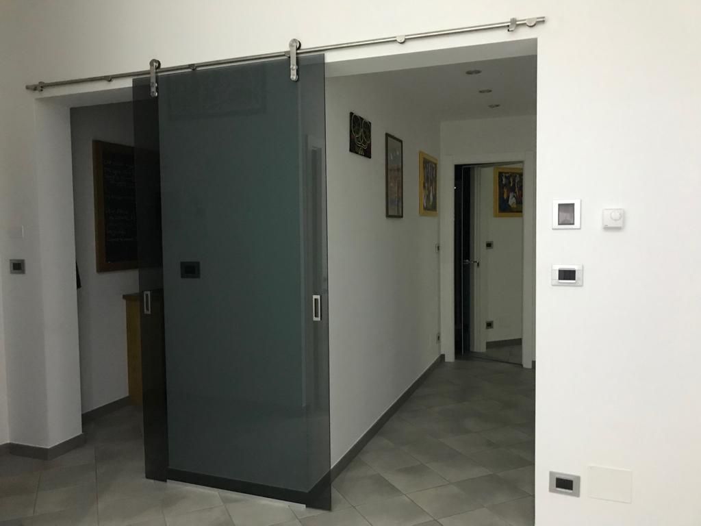 Porta scorrevole in vetro, grigia, su binario, che separa le stanze. 
