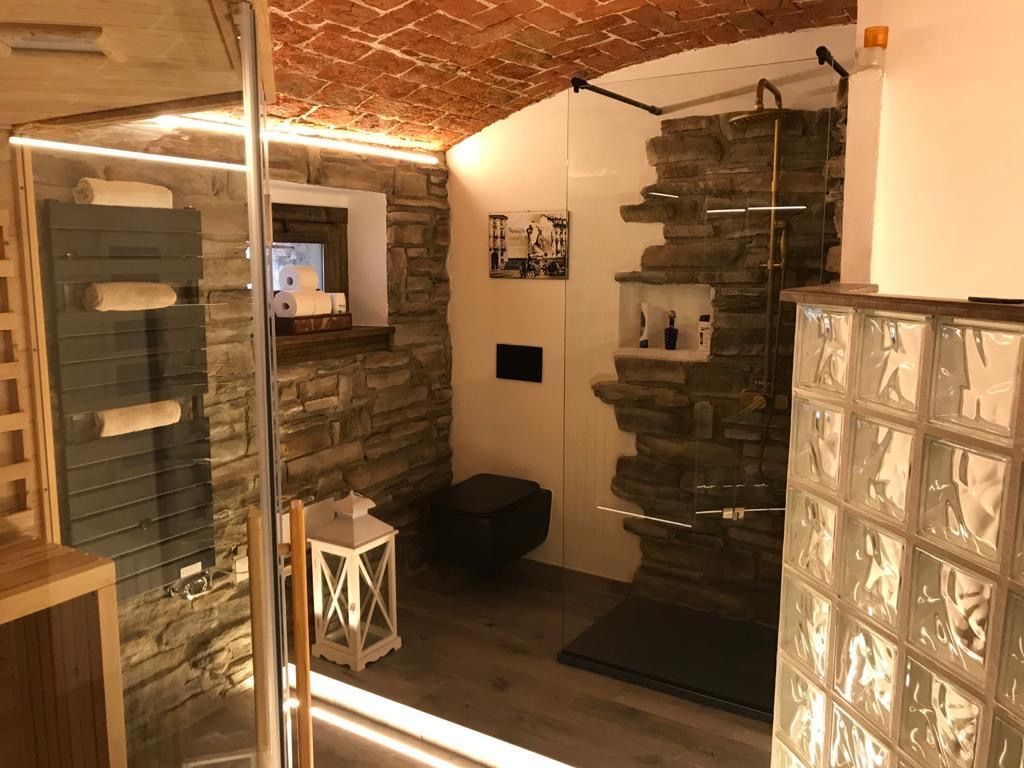 Bagno con pareti in pietra, soffitto in mattoni, doccia in vetro e scaldasalviette grigio.
