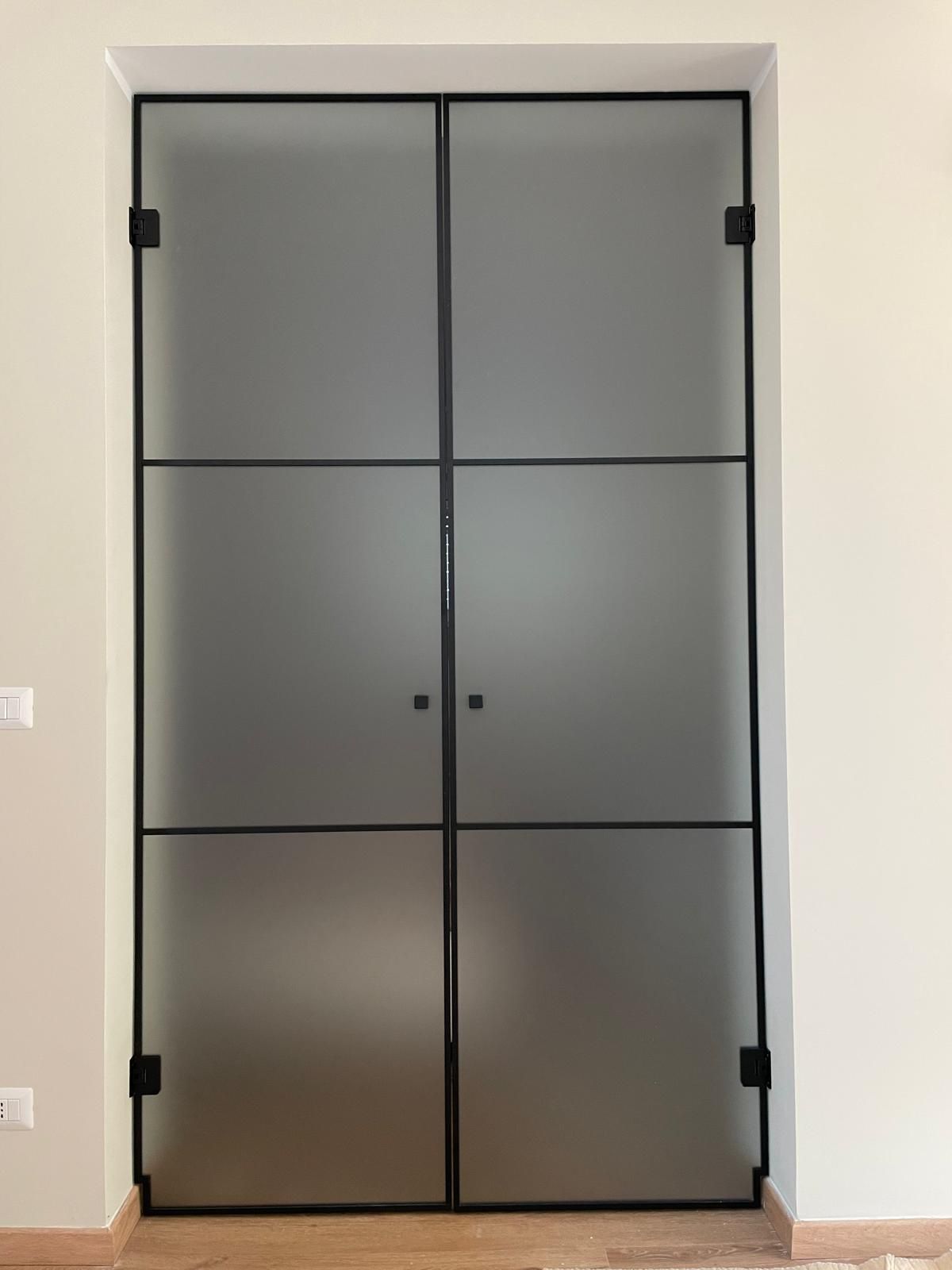 Doppie porte in vetro smerigliato con telaio e cerniere in metallo nero, inserite in un vano porta bianco.