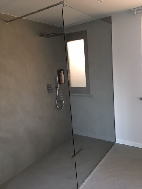 Box doccia moderno con pareti in cemento grigio, pannelli in vetro trasparente e una finestra.