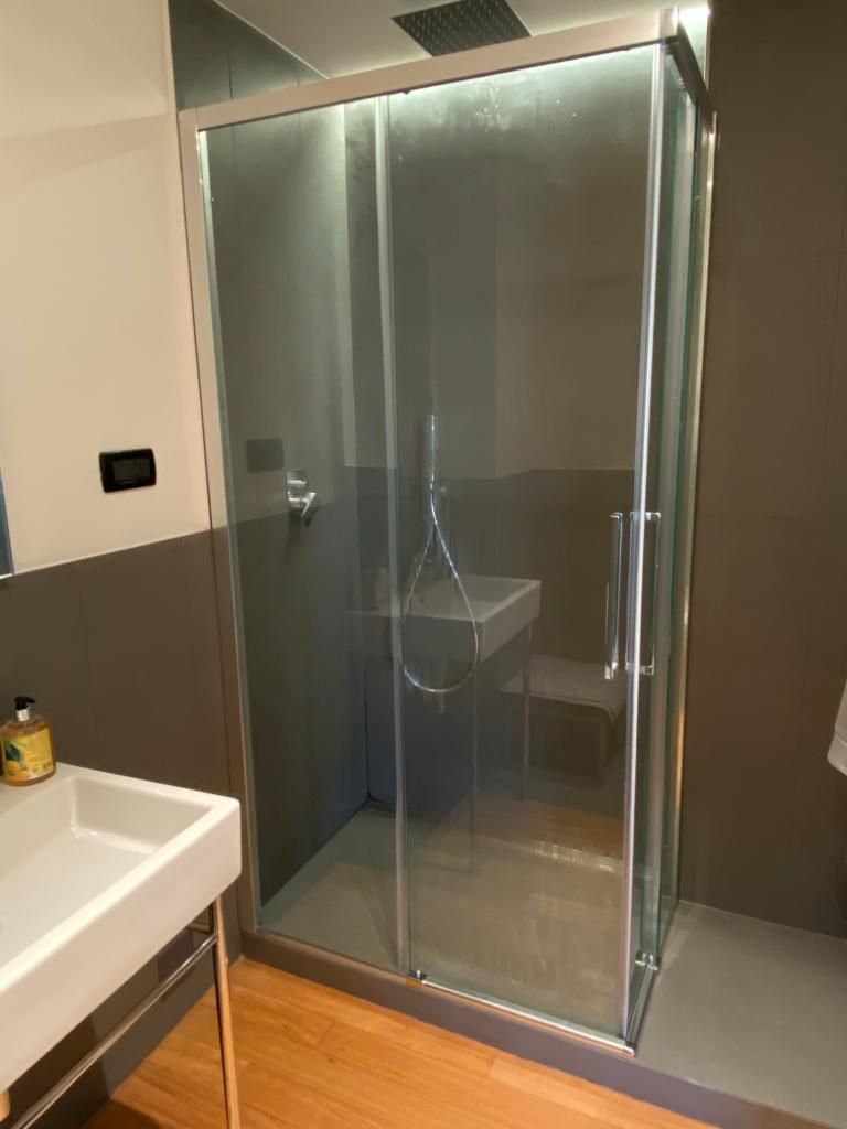 Box doccia in vetro in un bagno con lavandino e sanitari.