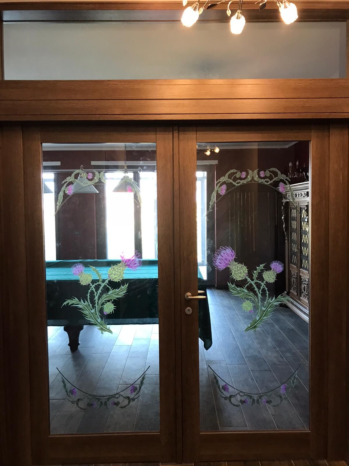 Doppie porte in legno con motivi decorativi a forma di cardo, che conducono a una stanza con un tavolo da biliardo.