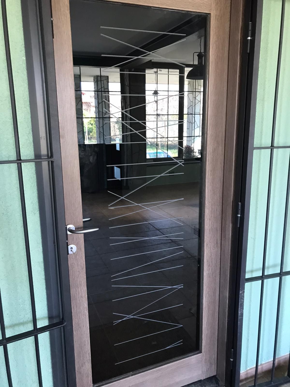 Porta in vetro con motivo a zig-zag e telaio marrone, circondata da barre verticali.