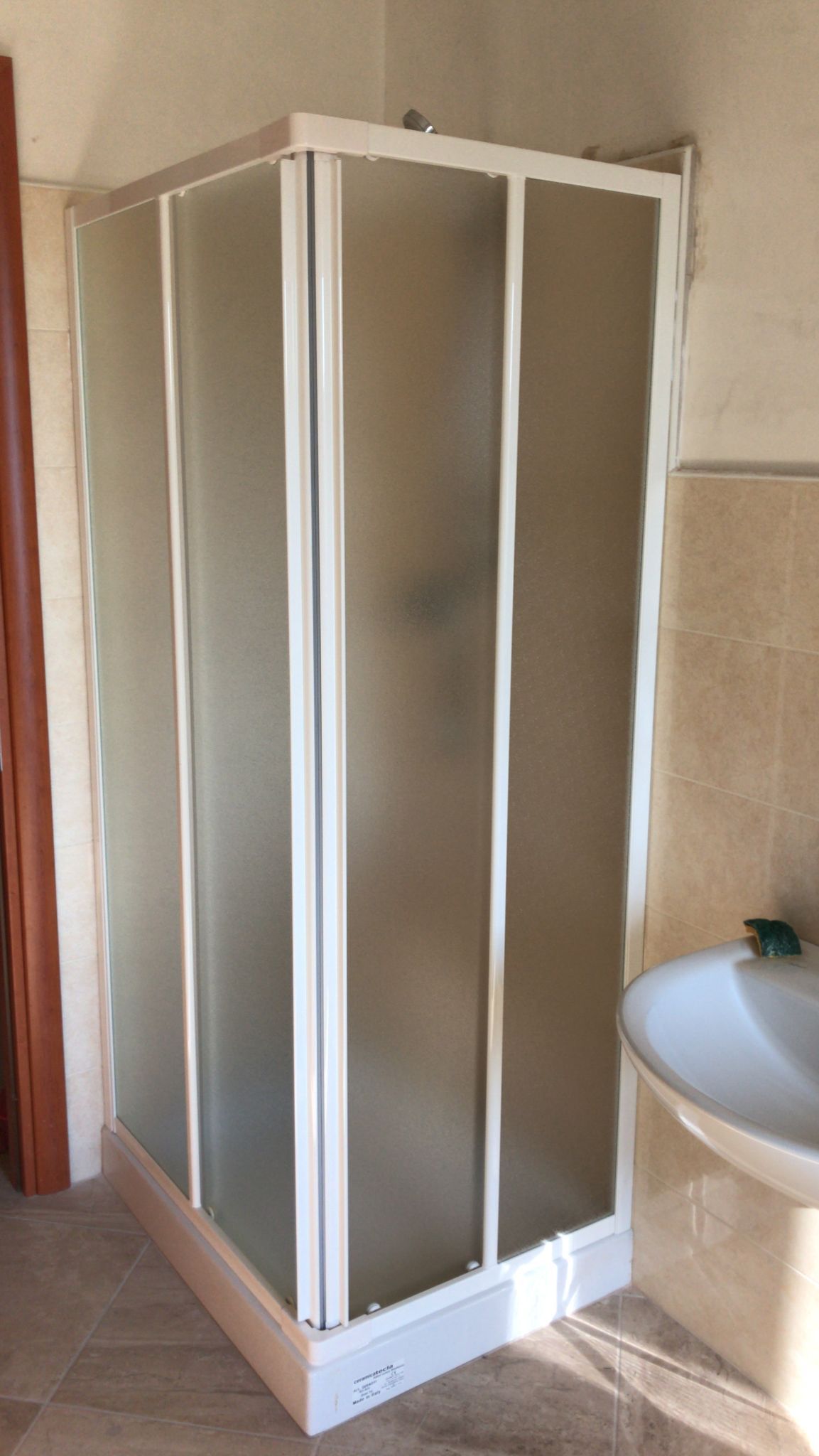 Box doccia con cornice bianca e porte in vetro smerigliato, accanto a un lavandino bianco.