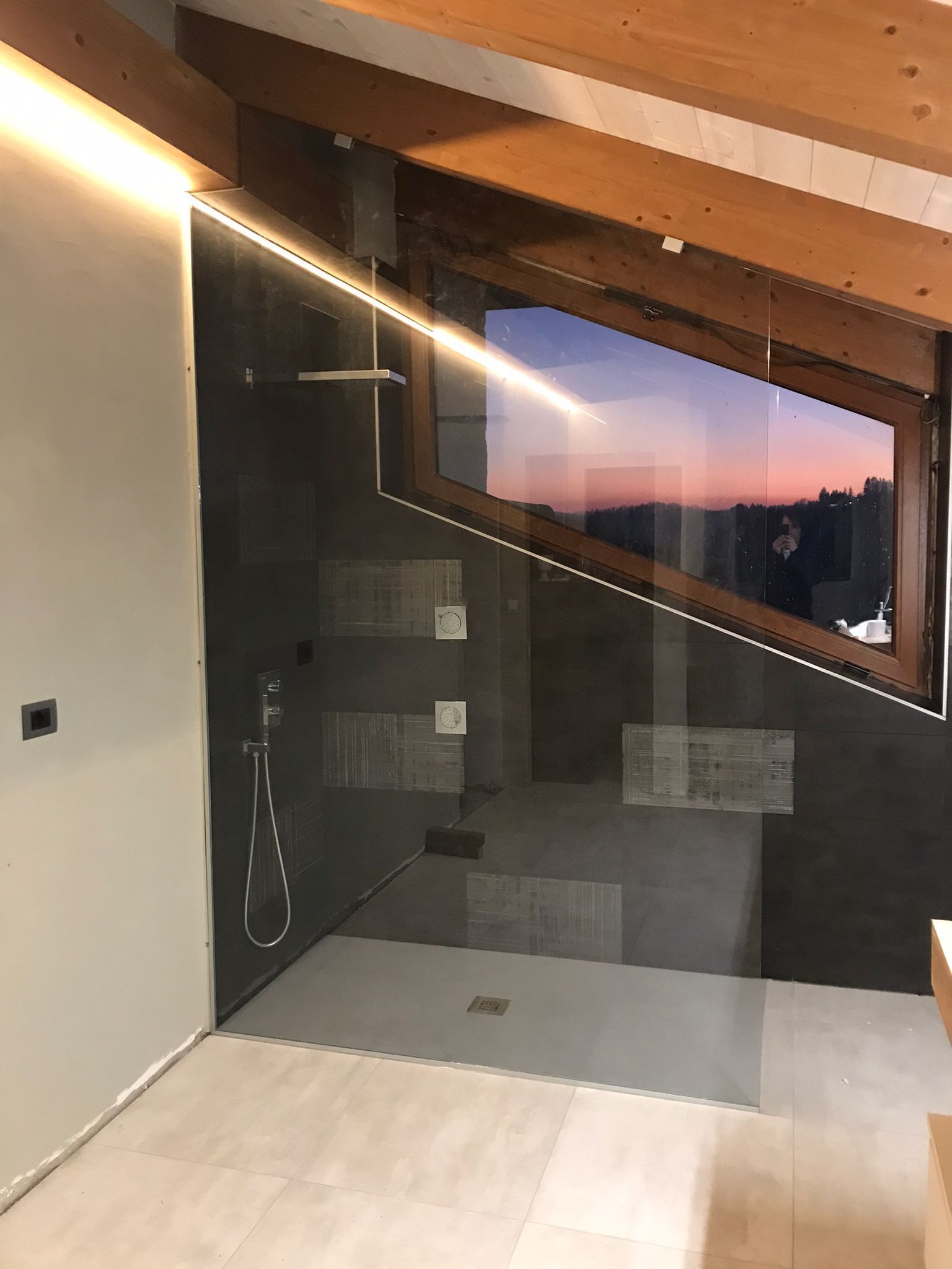 Doccia moderna con finestra ad angolo; piastrelle grigie, cabina in vetro, soffitto in legno.