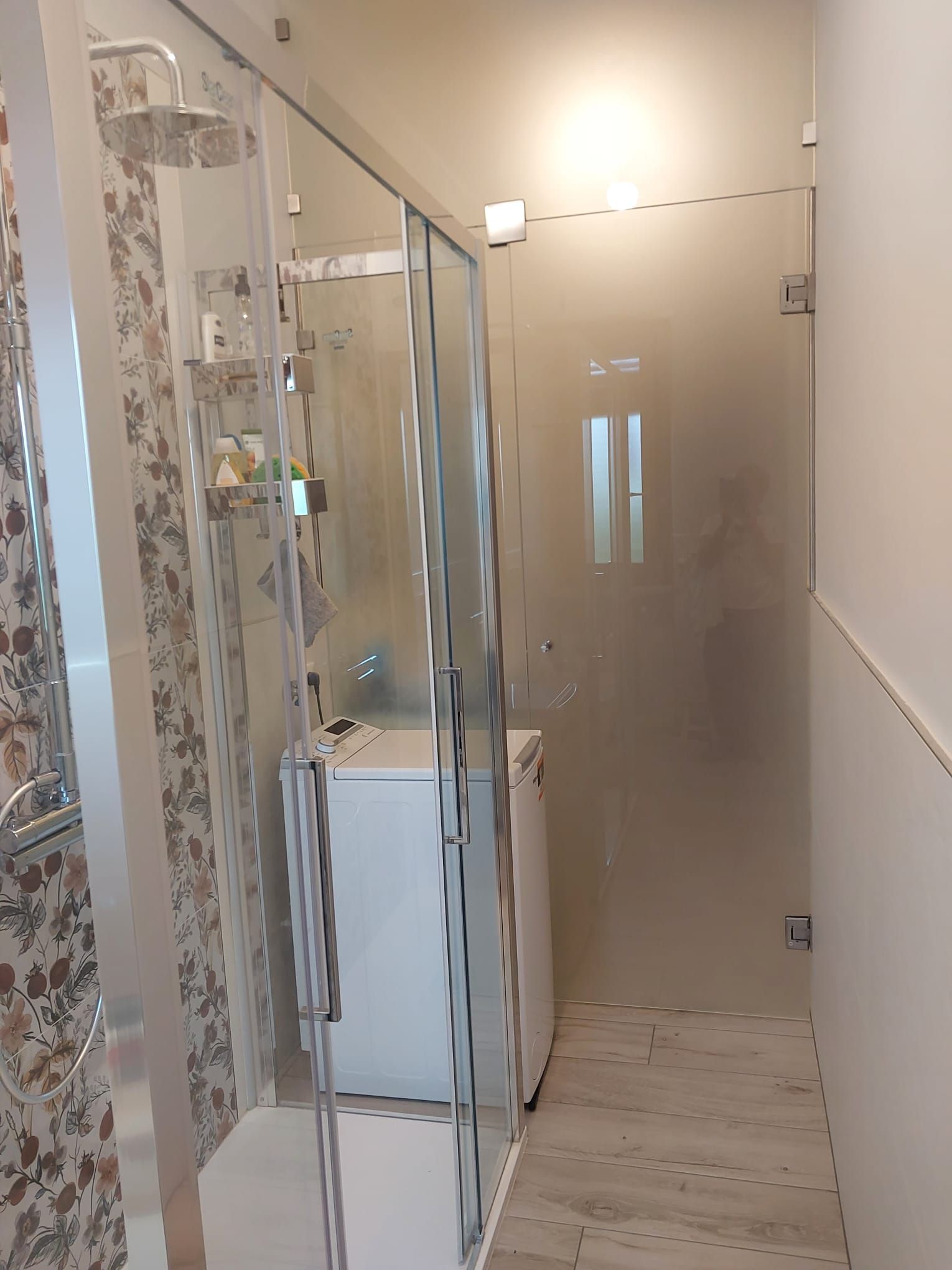 Box doccia con porte in vetro, pareti bianche e lavatrice all'interno.