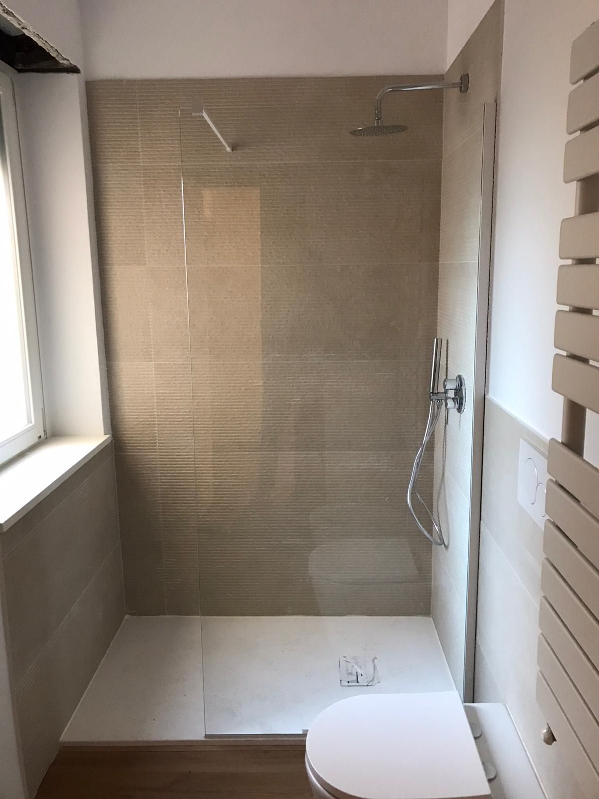 Piccolo bagno con cabina doccia. Pareti piastrellate beige, pavimento bianco, WC e portasciugamani.