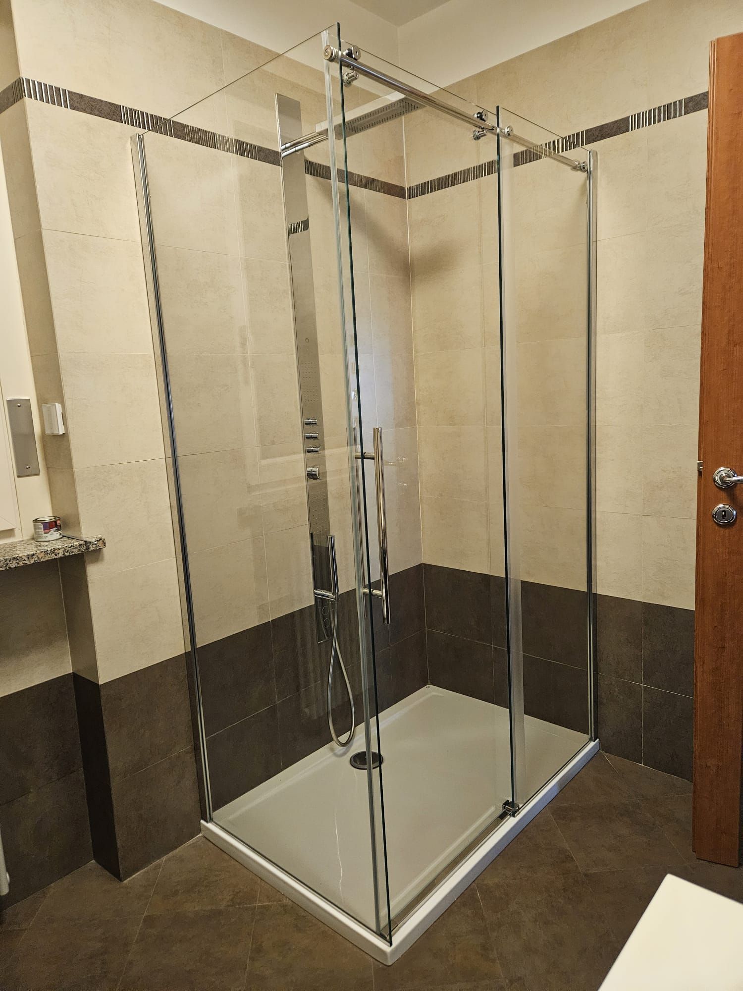 Box doccia in vetro in un bagno con piastrelle beige e marroni.