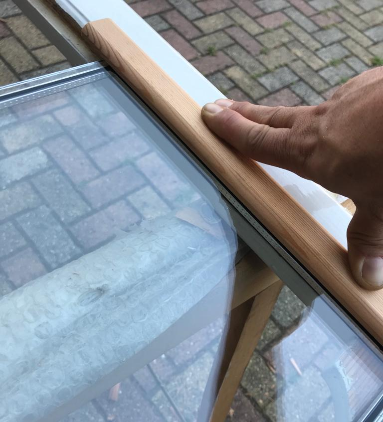 Mano che tiene una striscia di legno contro la finestra di vetro.
