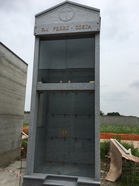 Colombario in granito grigio con sportelli in vetro per urne, in un cimitero.