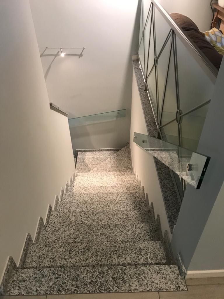Scala con gradini grigi screziati, ringhiera in vetro e metallo e pareti bianche, vista dall'alto.