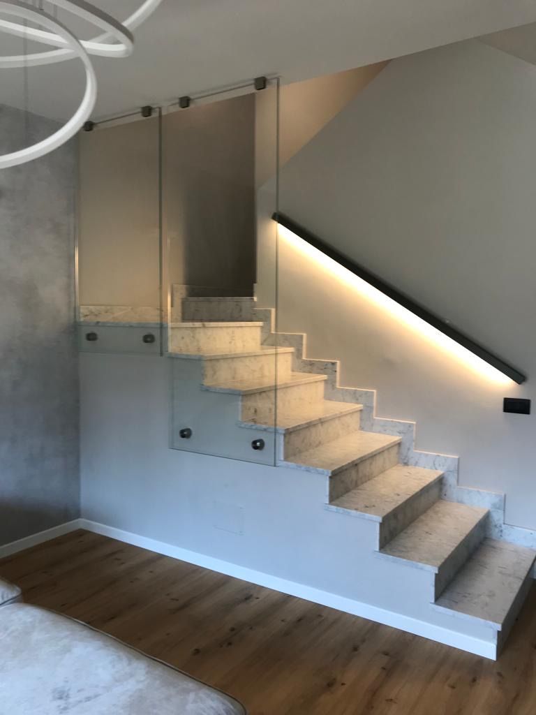 Scala con ringhiera in vetro e illuminazione integrata. Gradini in marmo e pareti chiare in un interno moderno.