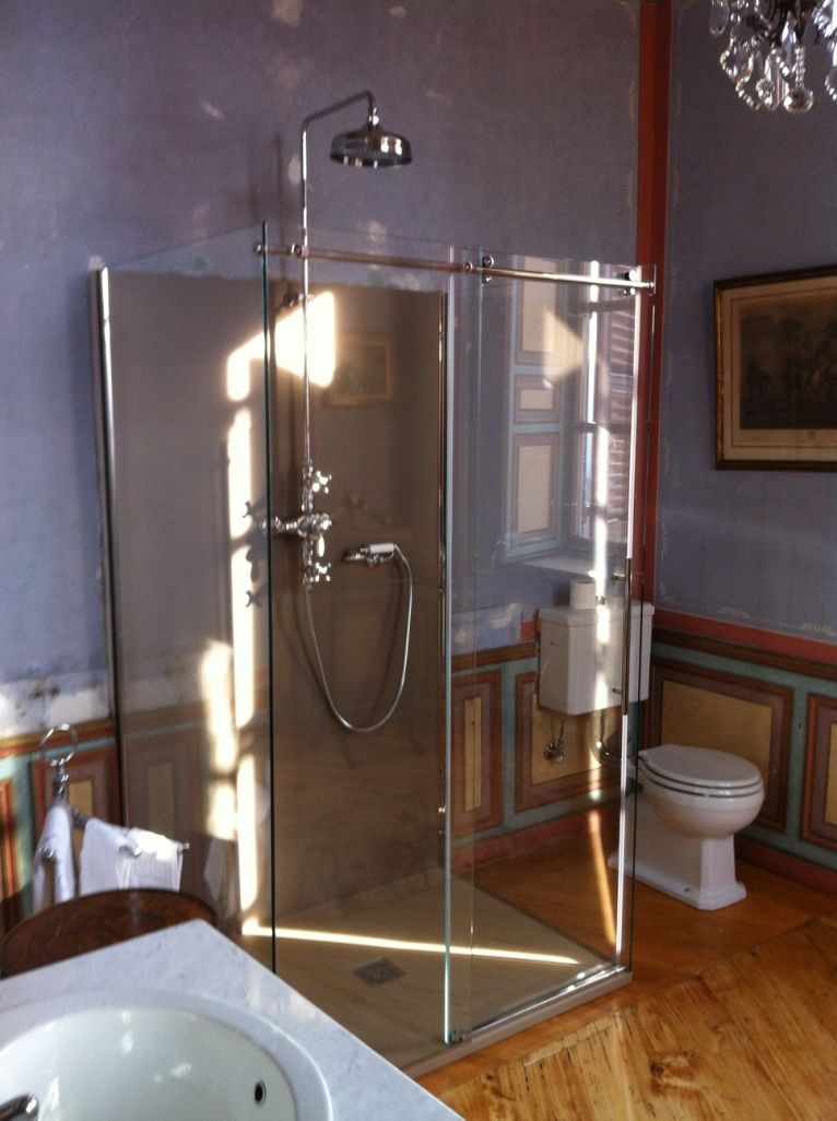 Doccia con porte in vetro e sanitari in acciaio inox in un bagno con WC e pavimenti in legno.