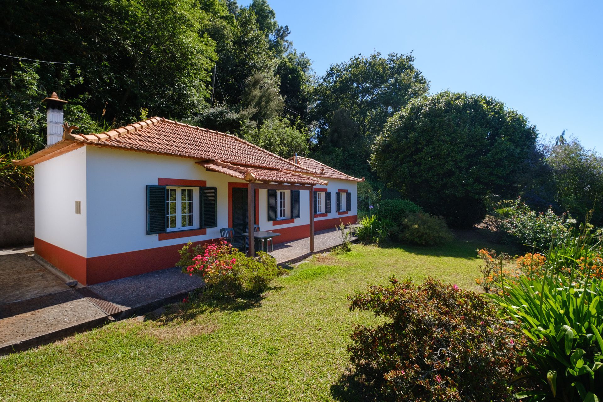 White house with orange trim and tile roof, green shutters, and lush green lawn.