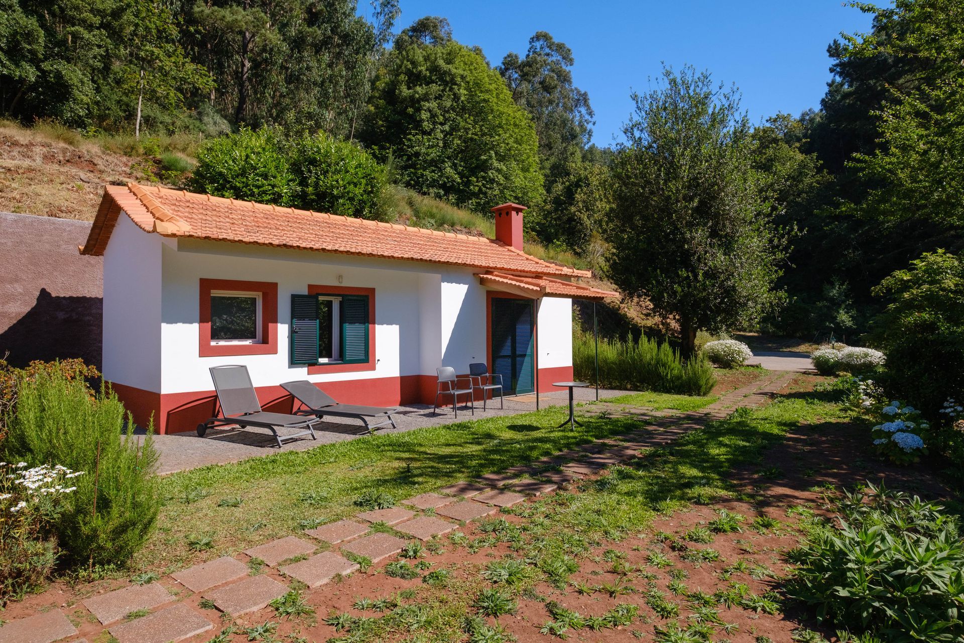 A white and red cottage with a red tile roof sits in a lush, green yard.