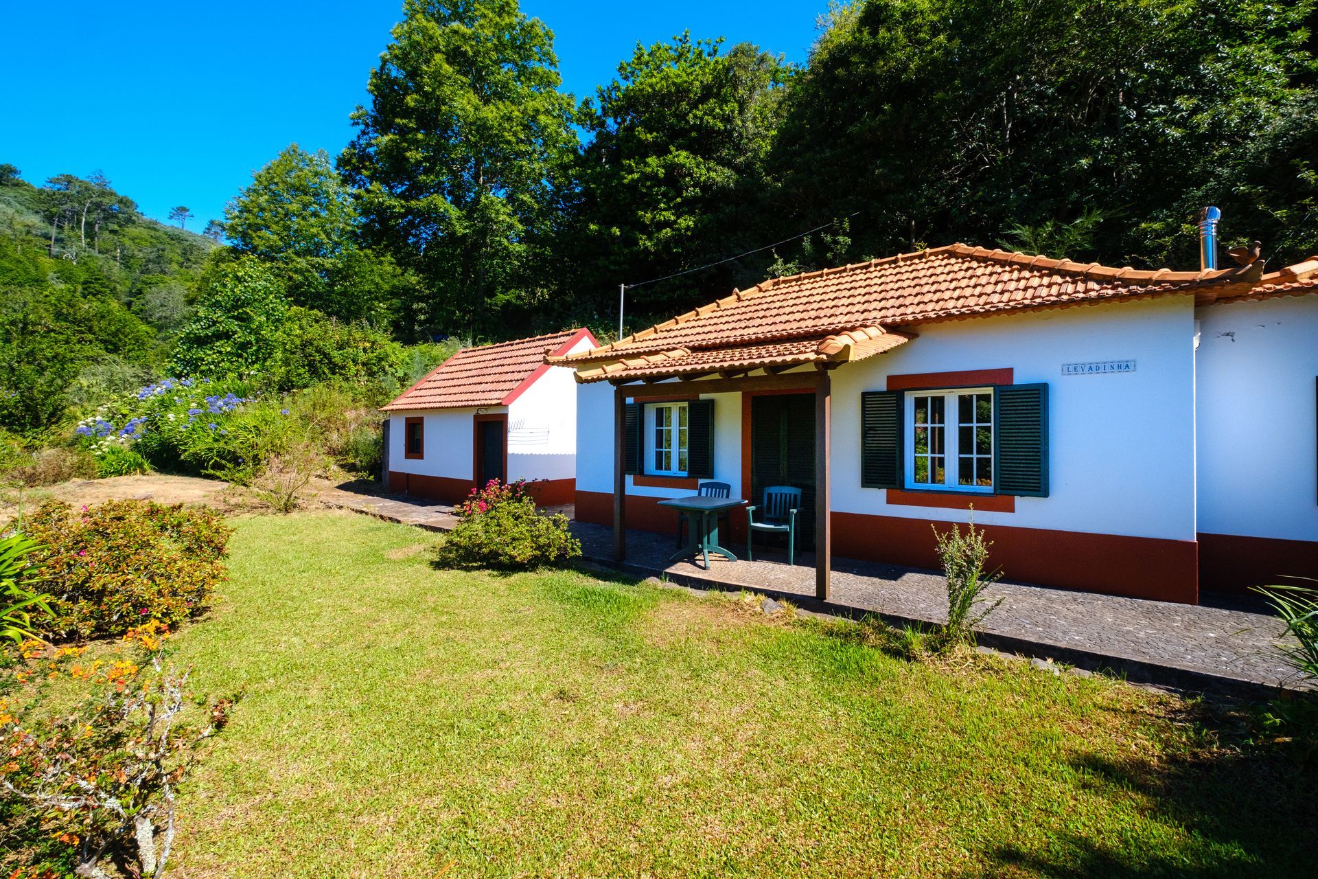Two white cottages with red trim and tile roofs in a green, sunny environment.