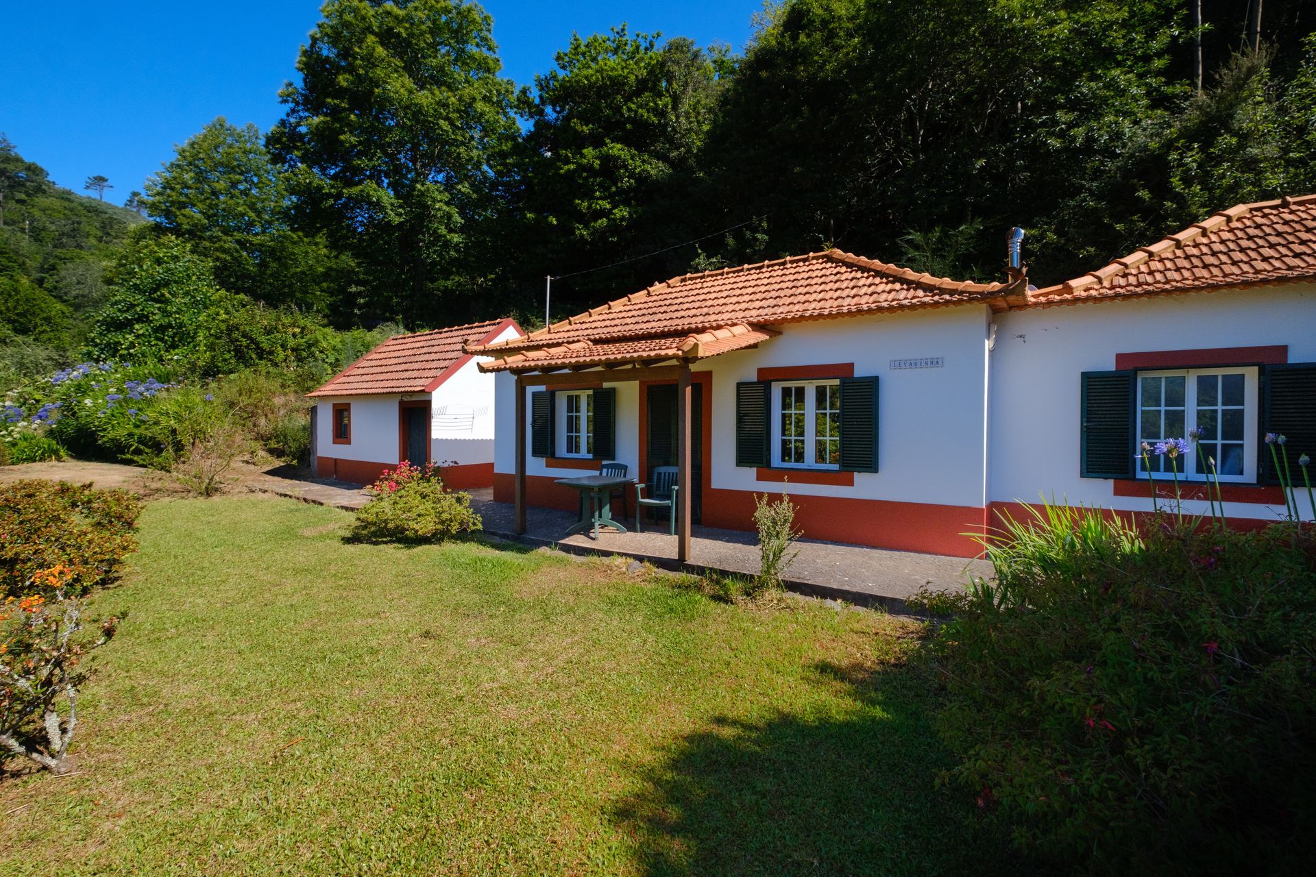 White bungalows with red trim and tiled roofs, set against a green grassy yard and lush foliage.