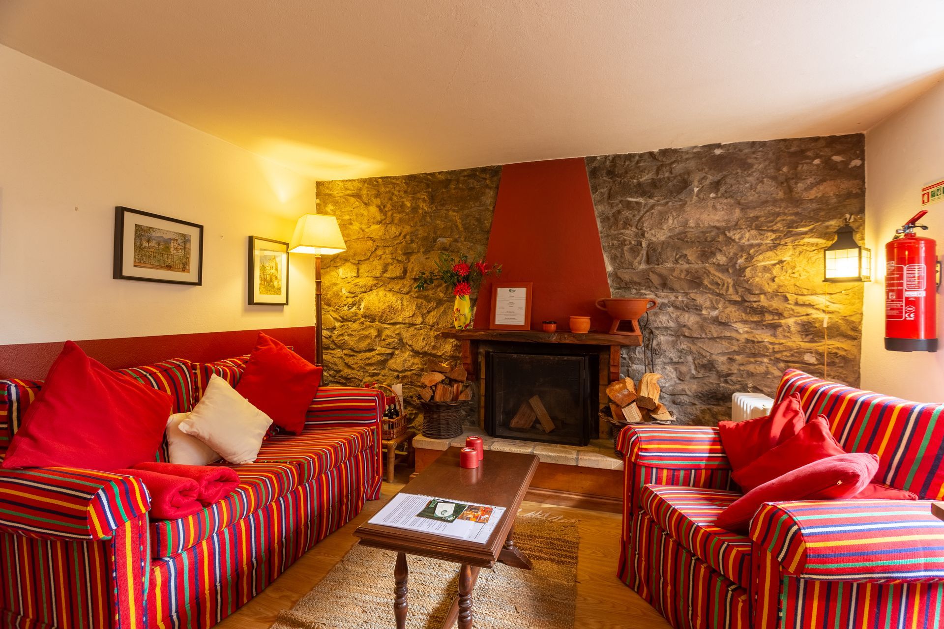 Cozy living room with red striped couches, fireplace, stone wall, and warm lighting.