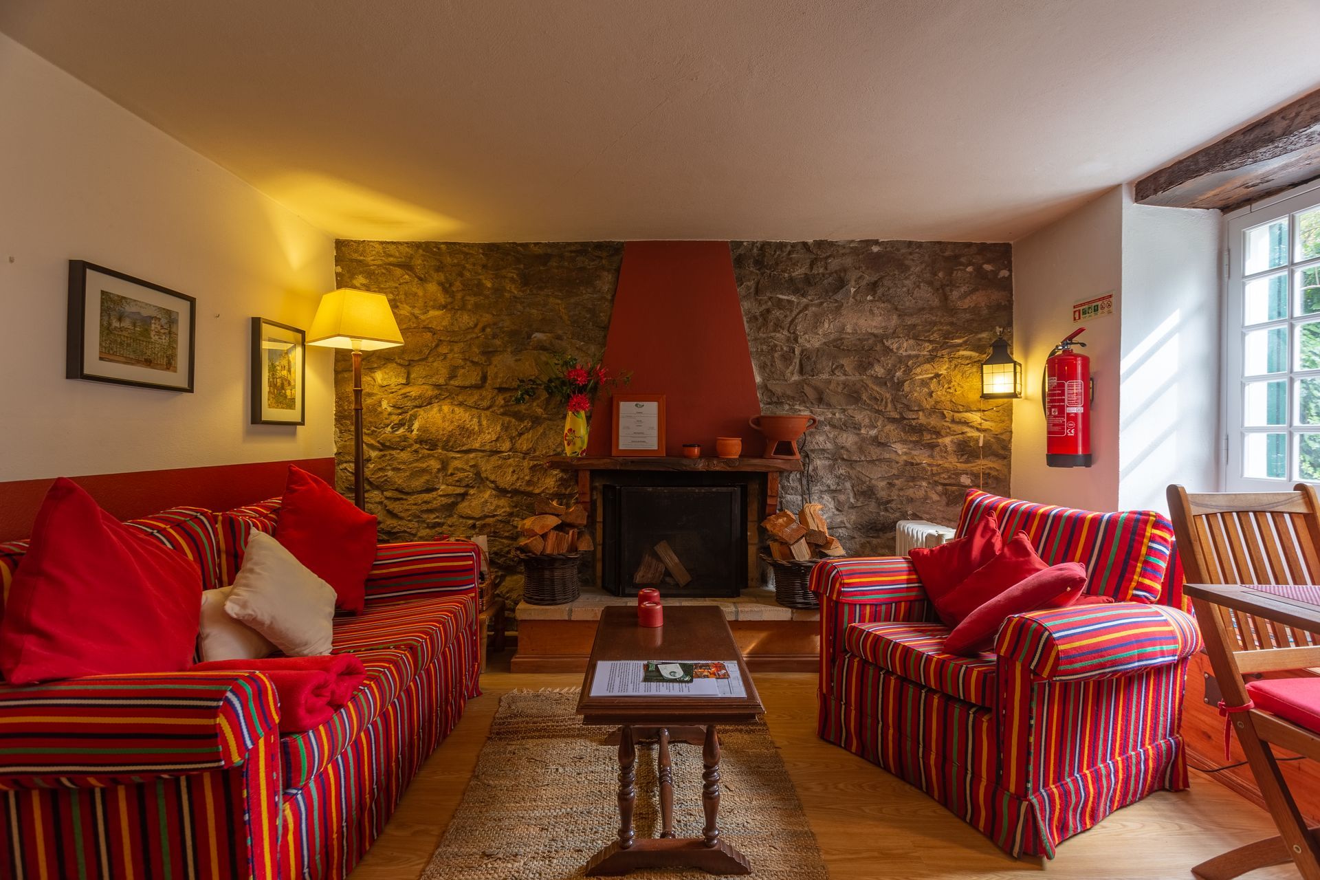 Cozy living room with red-striped sofas, stone fireplace, and small wooden table, bathed in warm lighting.