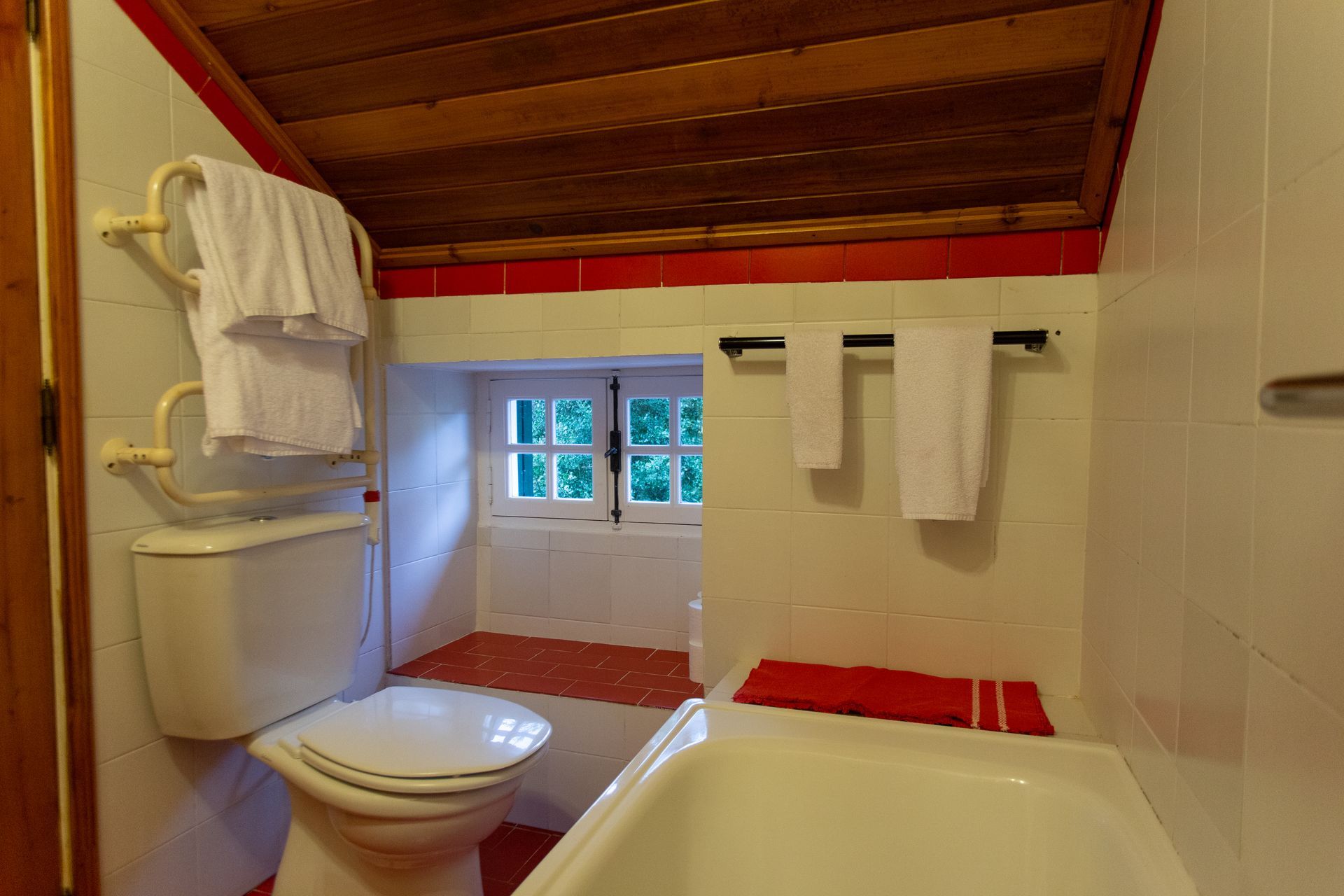 Bathroom with toilet, tub, and towels; a window is in the back.