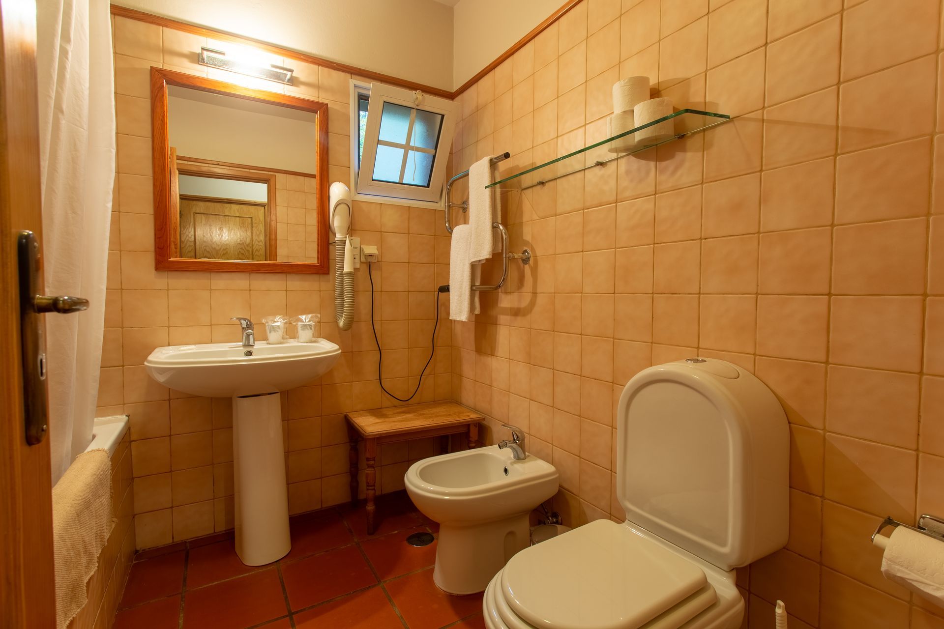 Bathroom with a pedestal sink, toilet, bidet, and beige tiled walls.