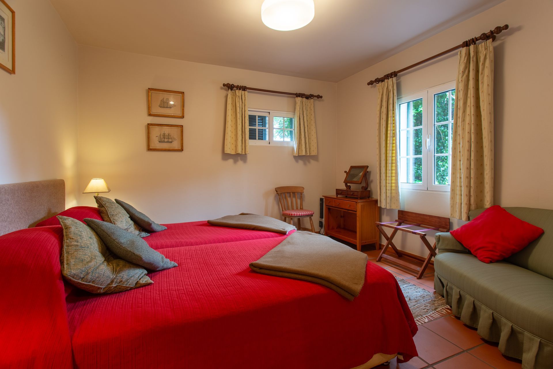 Bedroom with red twin beds, green sofa, windows, and beige walls.