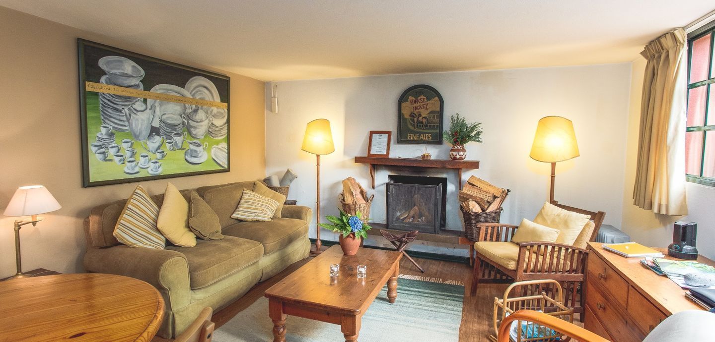 Cozy living room with a fireplace, sofa, chairs, and paintings. Warm lighting illuminates the space.