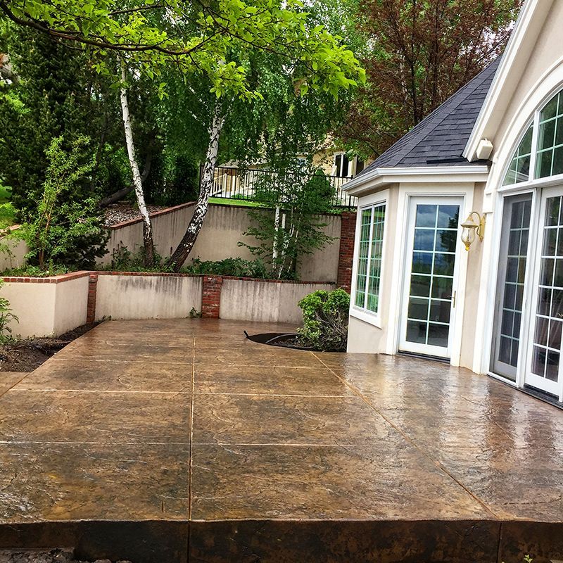 Wet stone patio beside a white house with French doors and trees in the background