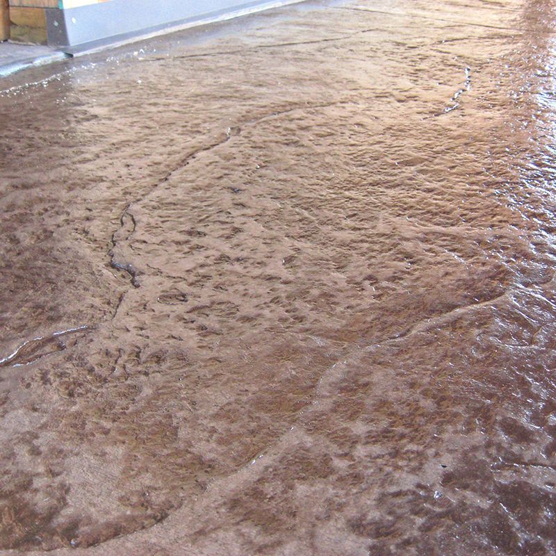 A muddy, wet floor with footprints and ripples of water near a wall.