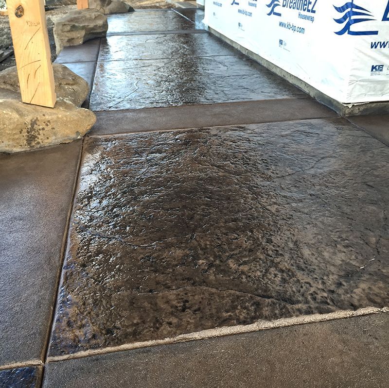 Wet concrete walkway under construction beside wrapped building materials and a wooden post