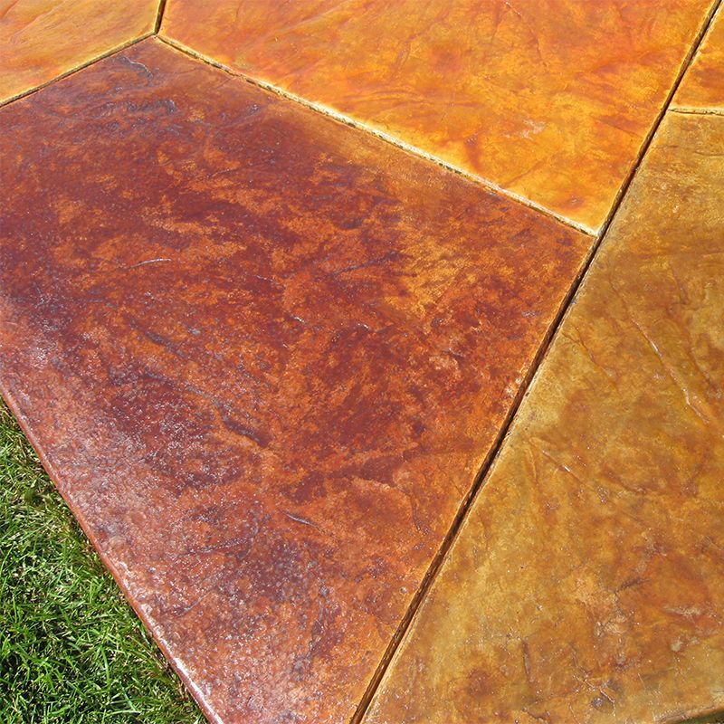 Close-up of textured orange and brown stamped concrete slabs beside green grass.