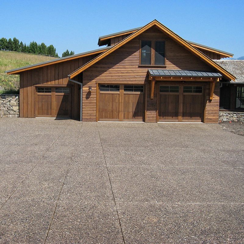 Wooden barn-style house with a large paved driveway under a clear sky