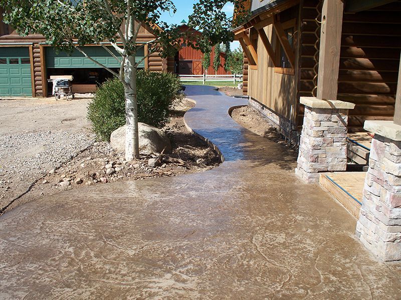 Fresh concrete walkway curving between log buildings and a tree in a construction area