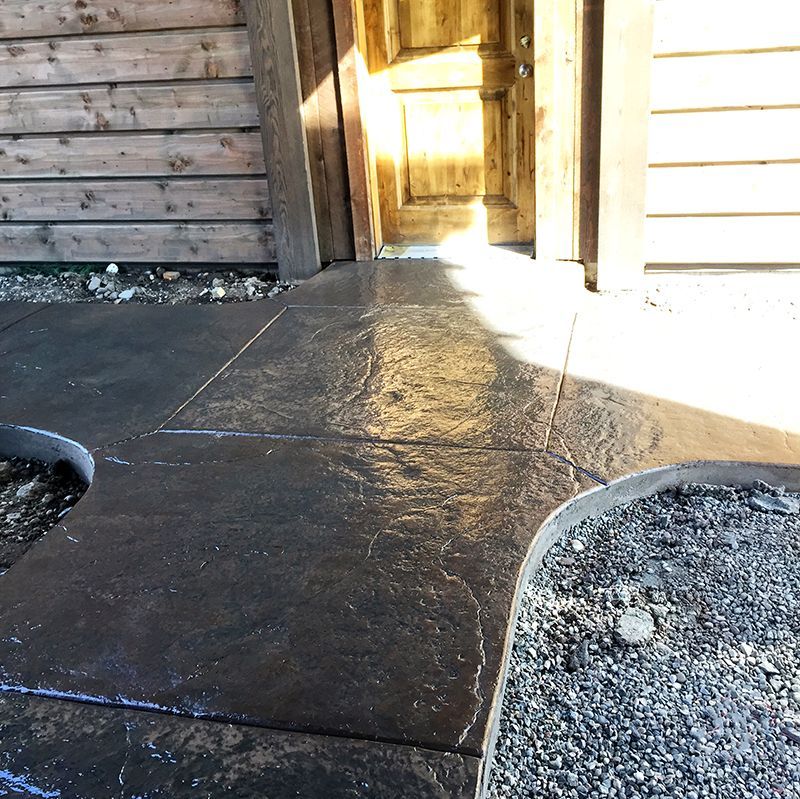 Concrete walkway between wooden walls, lit by bright sunlight, with gravel borders on both sides