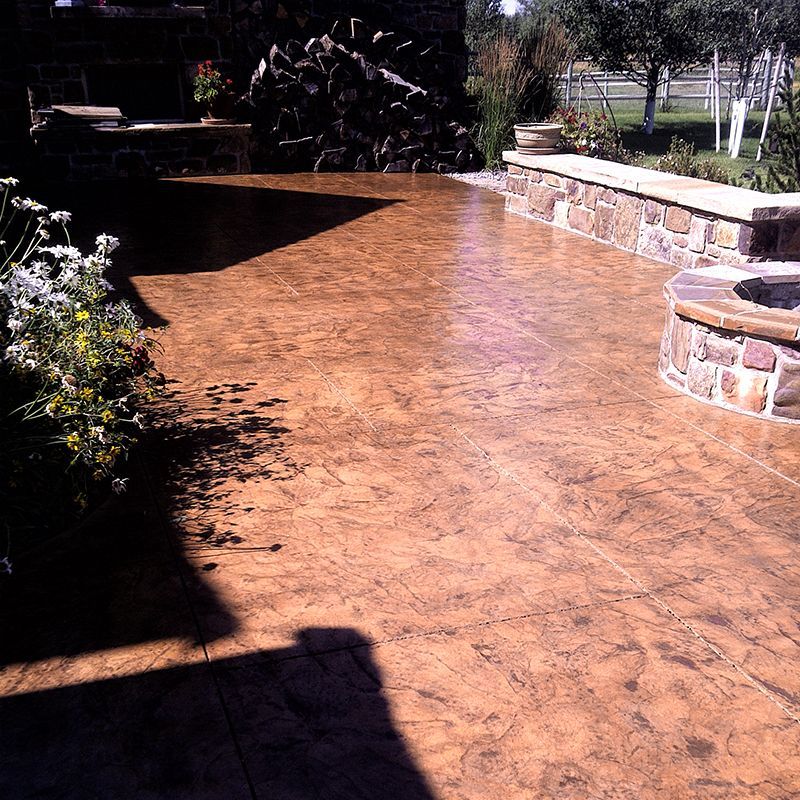 Sunlit stone patio with stamped concrete, a curved stone planter wall, and garden greenery.