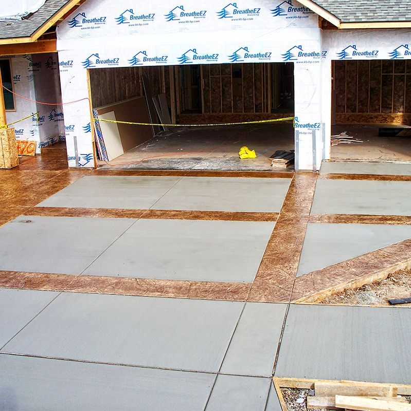 Concrete driveway and unfinished garage under construction, with wet pavement and building wrap visible.