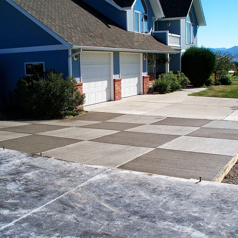 Blue house with white garage doors and a patterned concrete driveway in bright sunlight