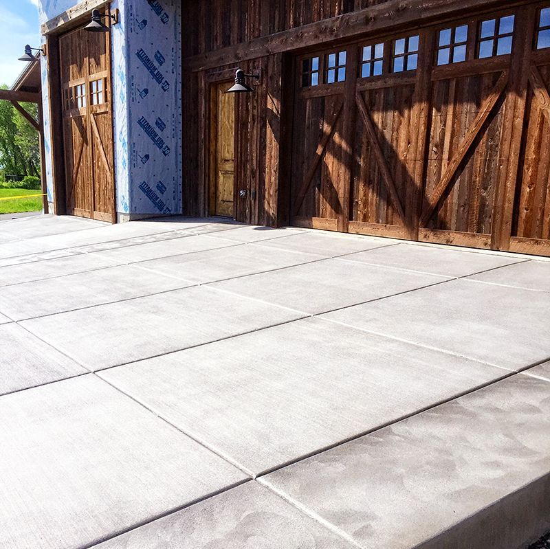 Concrete driveway in front of a wooden garage with large doors and blue trim