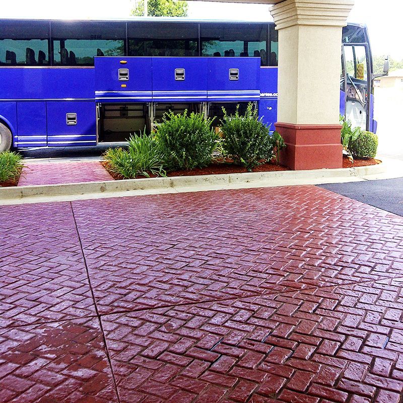 Blue bus behind a columned entrance, with shrubs and red stamped concrete in the foreground.