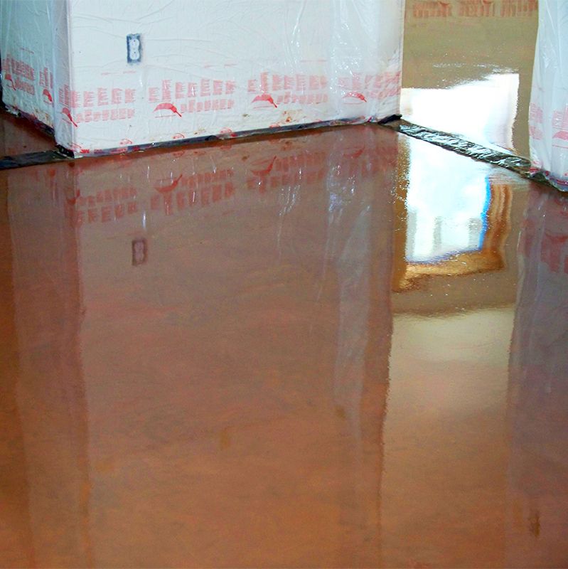 A shiny wet brown floor reflecting a window and stacked white boxes in a room