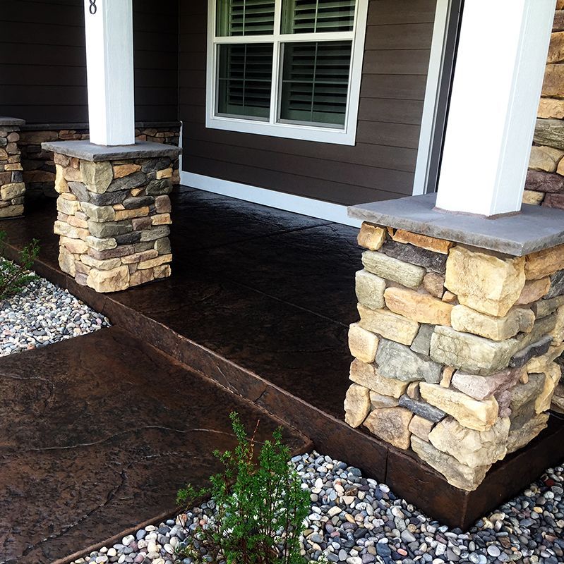 Stone porch pillars and dark brown siding on a house entry with stamped concrete steps and gravel landscaping