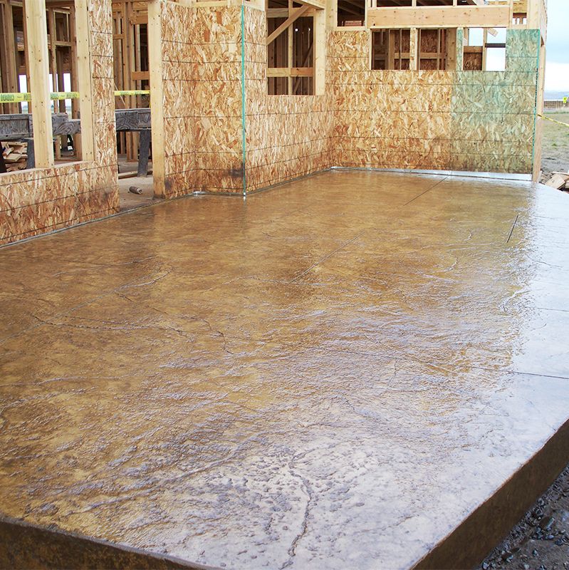 Freshly poured concrete slab beside unfinished wooden house framing.