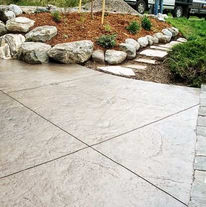 Concrete driveway beside a landscaped rock garden with stepping stones and shrubs